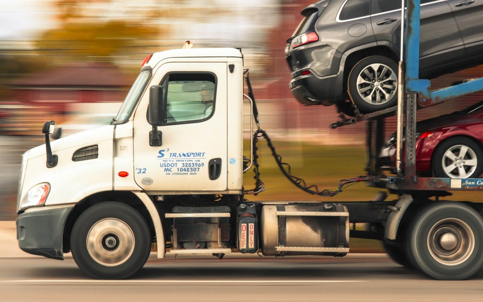 A car-hauler in motion on the road, carrying loaded vehicles, with USDOT and MC numbers on the cab