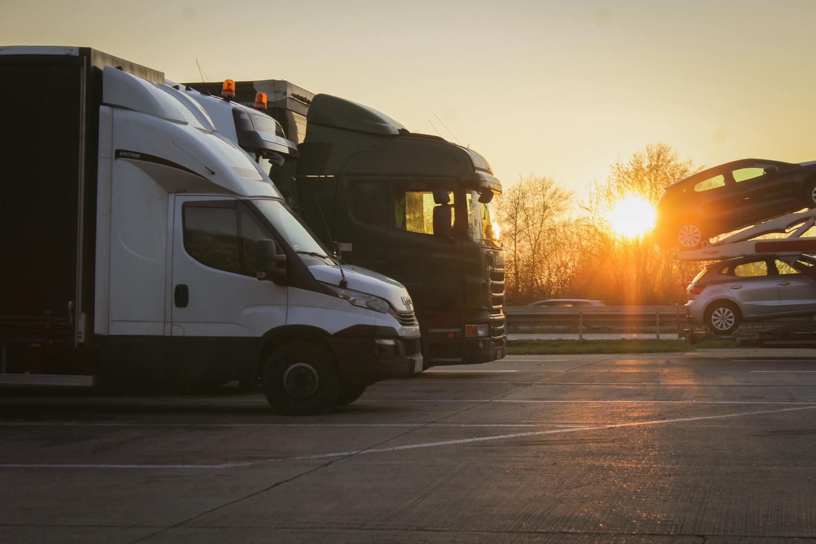 Car-hauler trucks at sunset, one loaded with vehicles, in a parking area